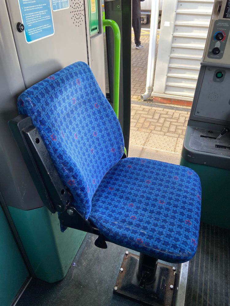 A class 170 drivers seat with a blue chequered moquette with stars or splodges in darker blue between the lines. Some of the stars are red edged.