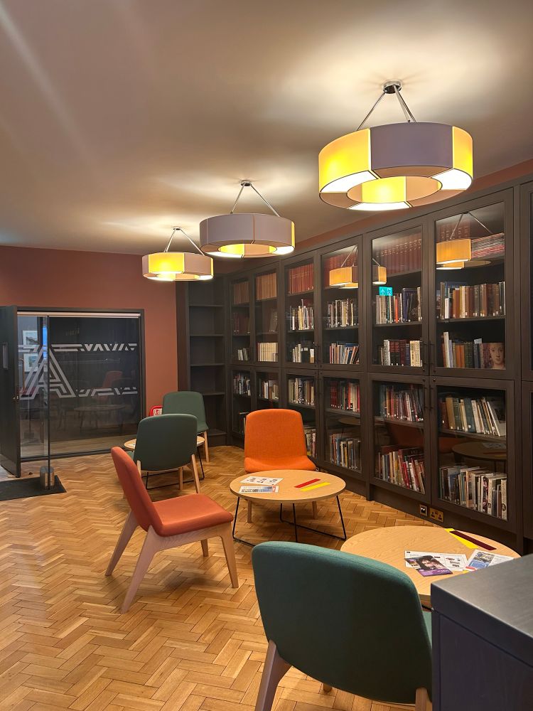 A library with shelves of books,  a parquet floor, and orange and green chairs