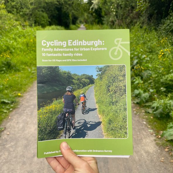 A hand holding up the Cycling Edinburgh guidebook: Family Adventures for Urban Explorers - 10 fantastic family rides.