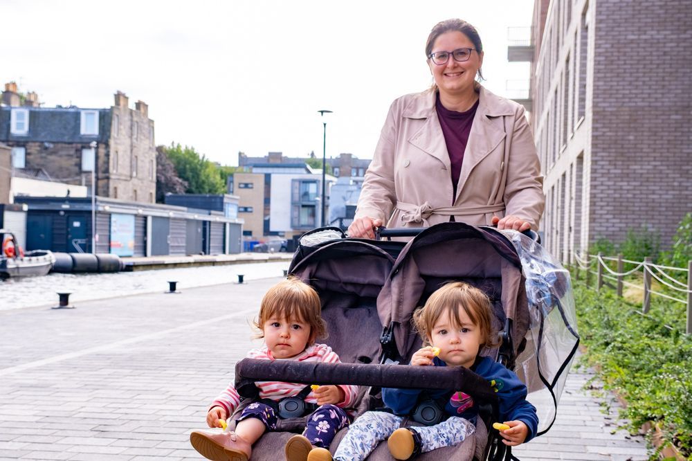 Twin girls sitting in a double buggy, pushed by their mum on the newly improved canal towpath in Fountainbridge, Edinburgh.