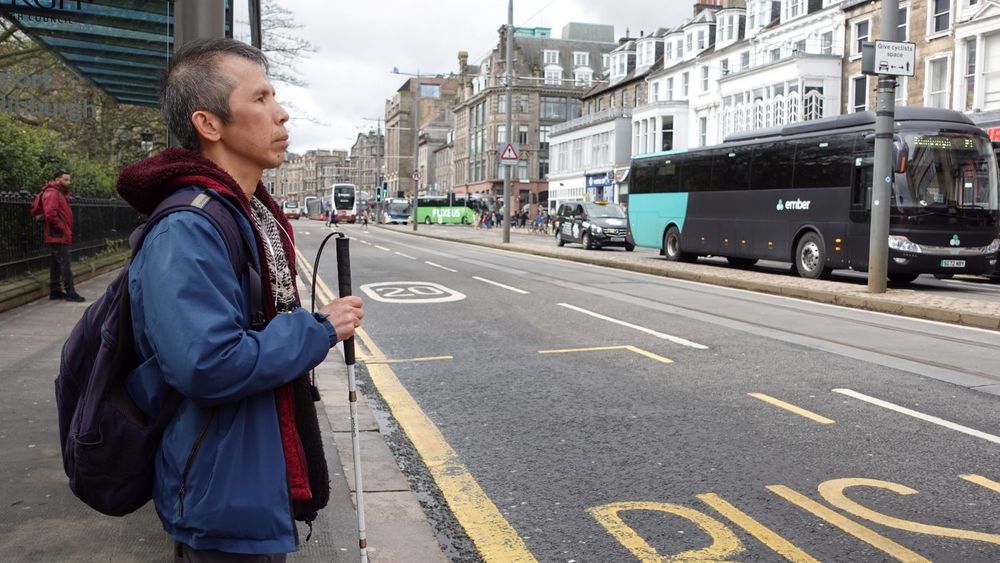 Visually impaired man standing at a bus stop on Princes Street in Edinburgh.