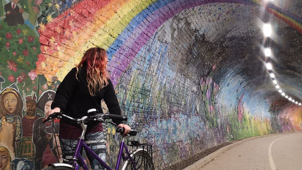 Person standing with a bike in Colinton Tunnel, admiring the artwork on the tunnel walls.