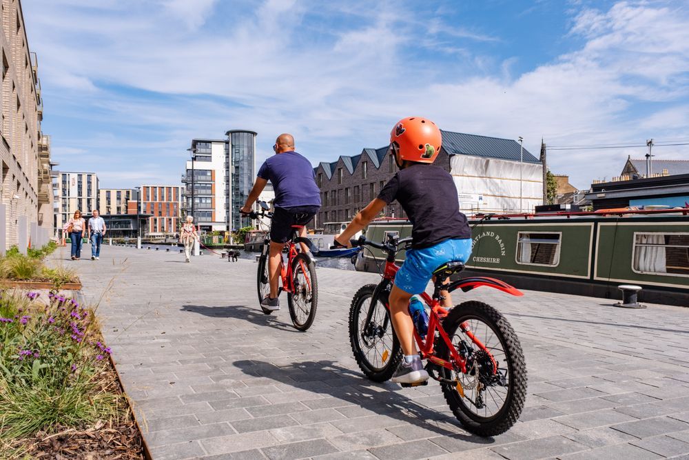 The newly improved canal towpath in Fountainbridge, Edinburgh. A man and boy are cycling in the foreground, and others are walking in the background.