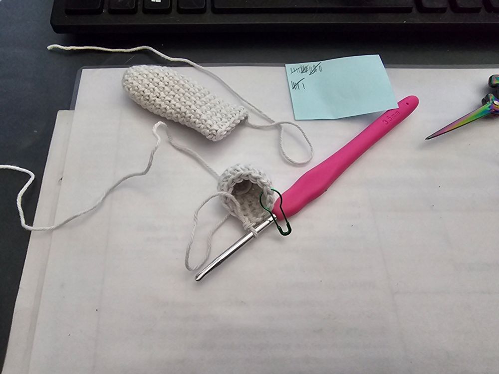 Häkelstücke auf einer weißen unterlage, daneben ein Zettel mit einer Strichliste zum zählen der gehäkelten Runden. Benutzt wird eine pinke Häkelnadel