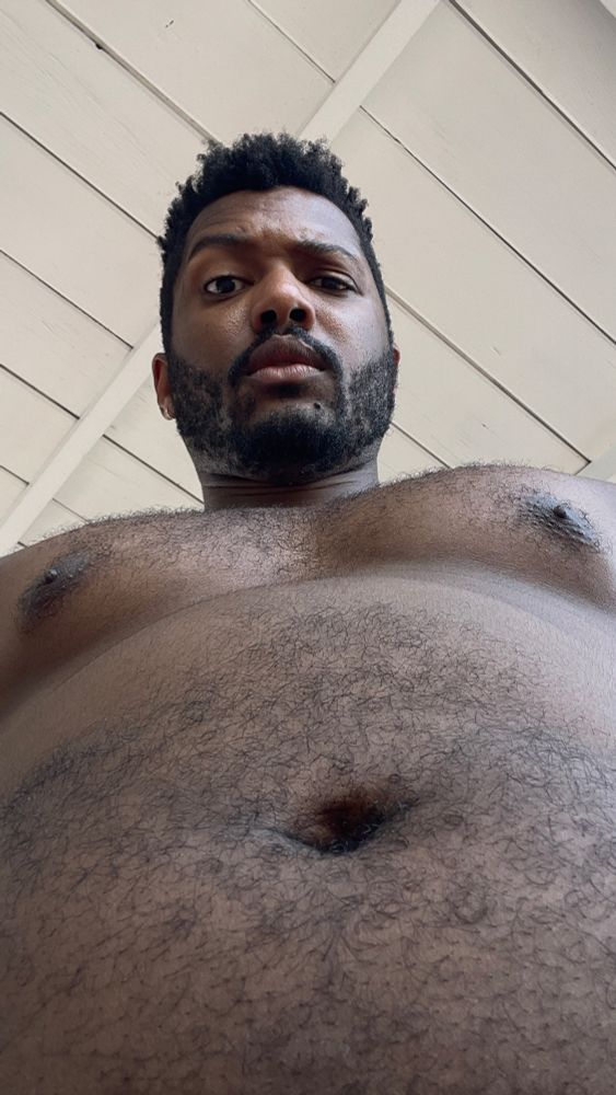 a bottom up selfie of a shirtless-torso’d figure looking down at the camera, his eyebrow is cocked