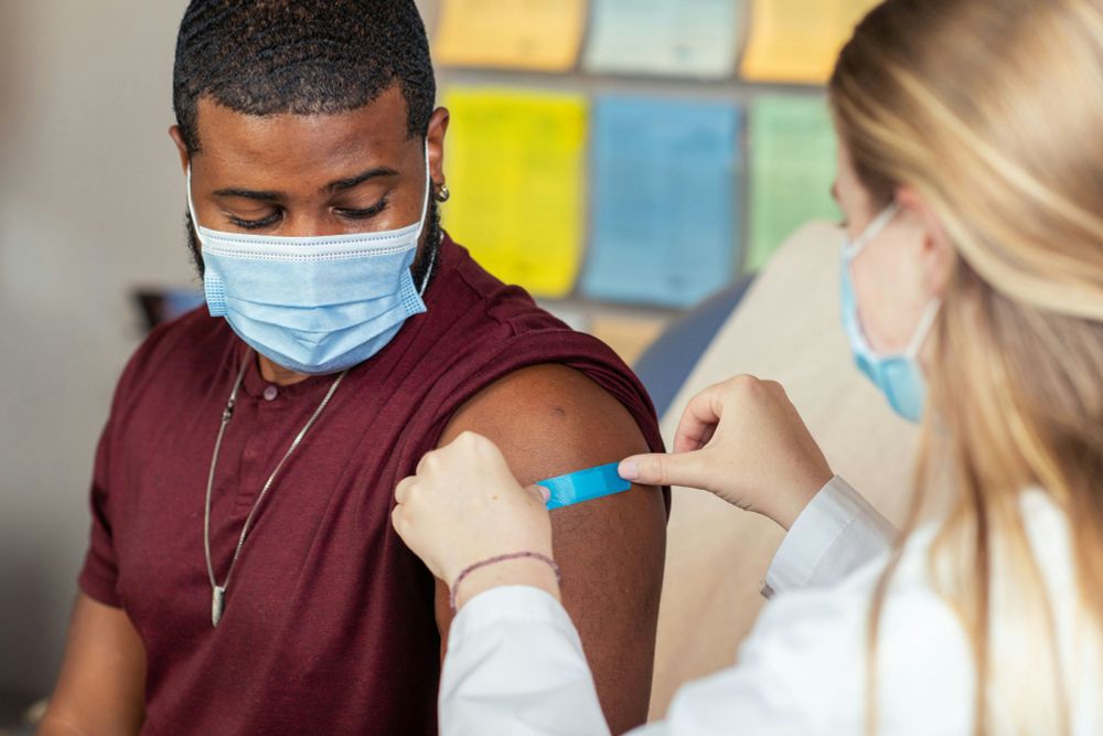 A health care provider places an adhesive bandage on the injection site of a patient who just received a vaccine.