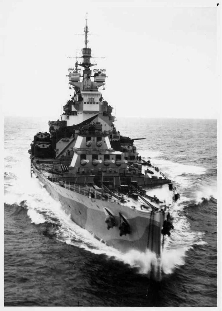 HMS Howe, and Brittish Battleship of the second world War, steams ahead. Image is from the bow, slightly from starboard. Visible are the forward turrets, one quad ahead, one double superfiring behind. 