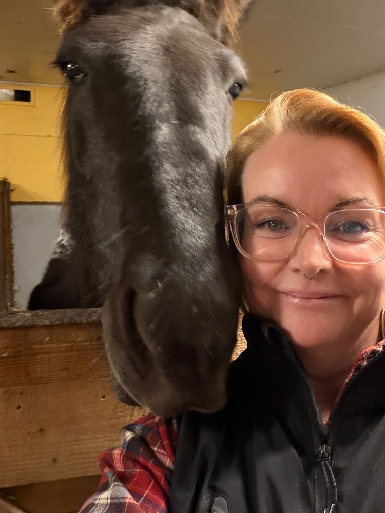 En selfie med en mörkt brun islandshäst och en tjej med glasögon