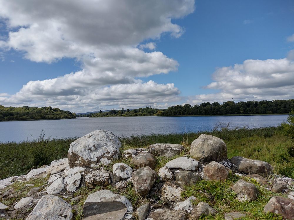 View over a lough with stones in the foreground, clouds and blue sky.
