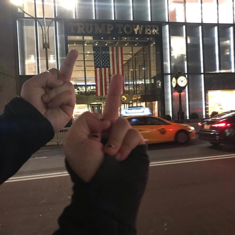 Two hands from two separate individuals flipping off Trump Tower in New York.