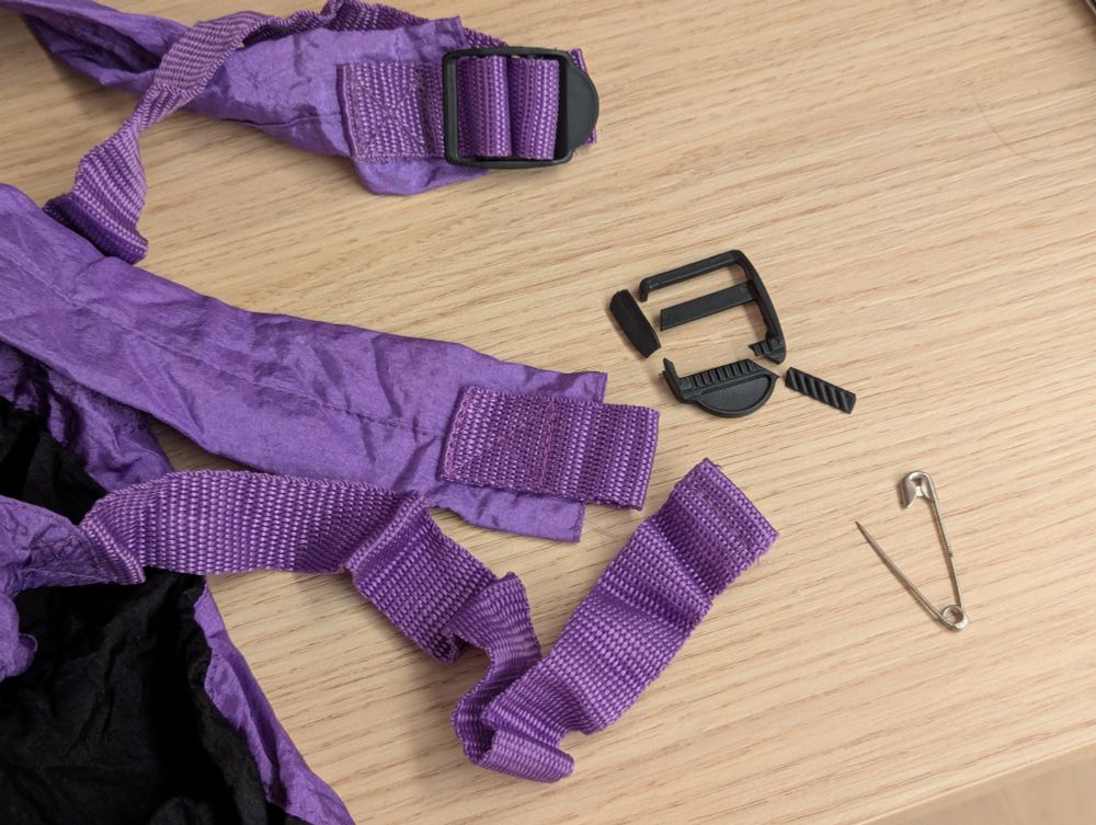 Photo of some rucksack straps with a broken plastic tri-glide slide buckle, and a replacement safety pin. 