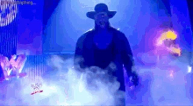 a man in a hat is walking through a smokey area with a w logo in the background