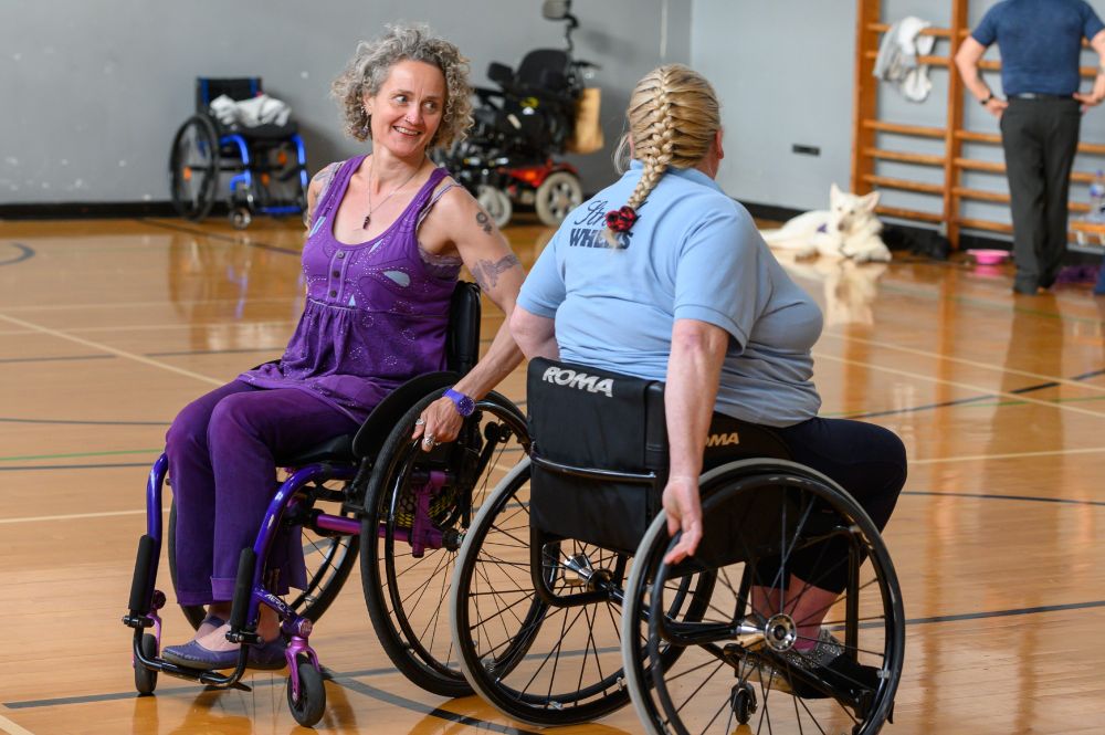 Image of a person in a wheelchair dancing with their partner in a sports hall.
