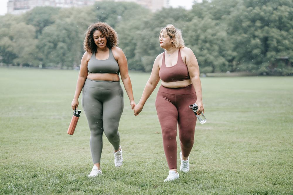 Two smiling people walk through a green field while wearing workout clothing