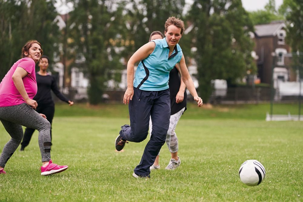 Adults play football in a green park while wearing sports gear.