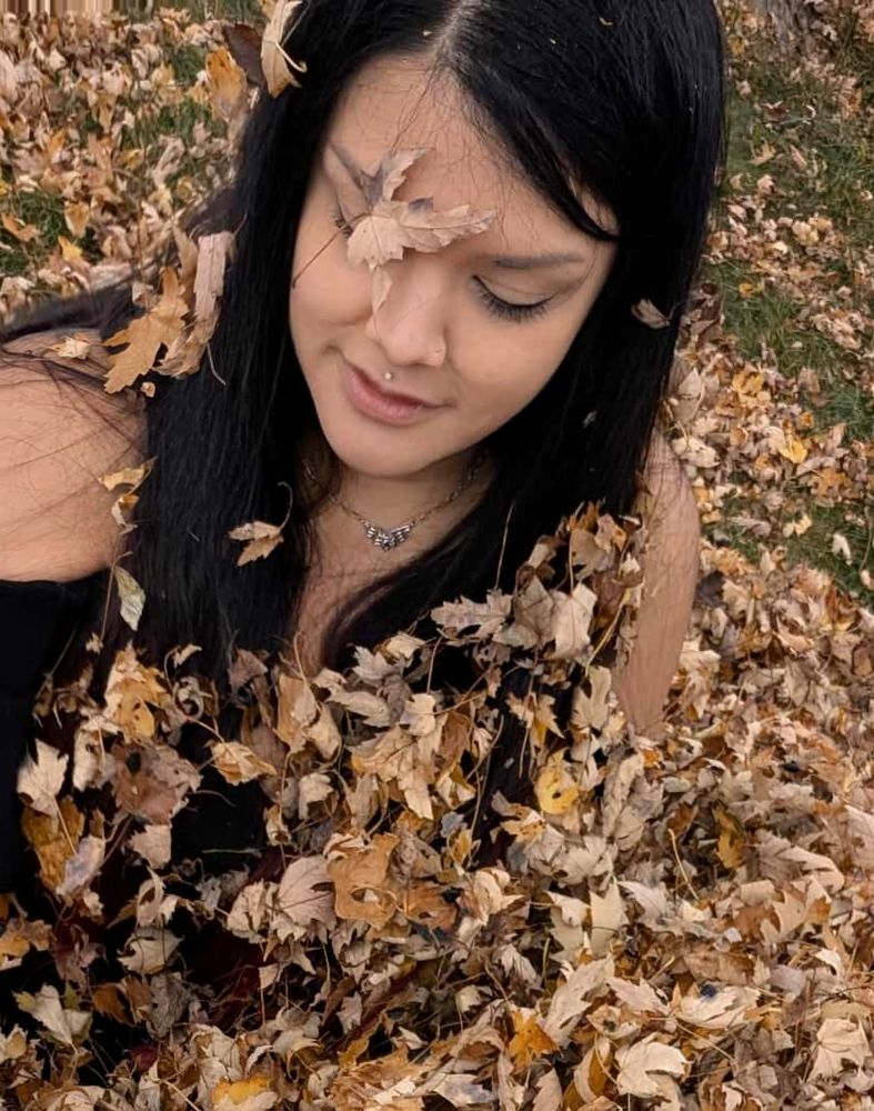 Me sitting in a pile of leaves. There's a leaf on my face and leafy crumbs in my hair. Also if you're reading this, hi you're cute!