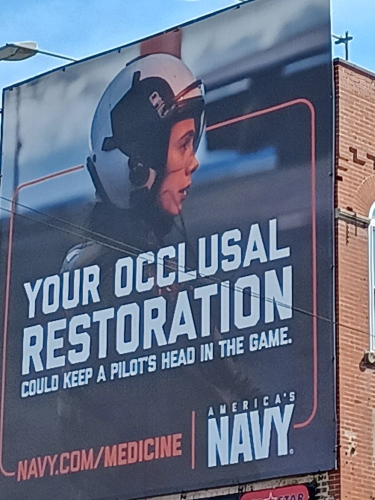 US navy propaganda billboard, text reads "Your occlusal restoration could keep a pilot's head in the game, navy.com/medicine, America's NAVY." Picture is of a woman pilot's profile. Belmont Avenue, Chicago.