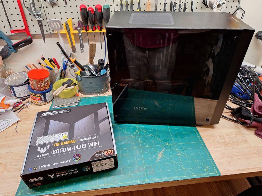 My gaming pc tower on my workbench, with the unopened box for the new motherboard next to it. Lots of tools are scattered around.