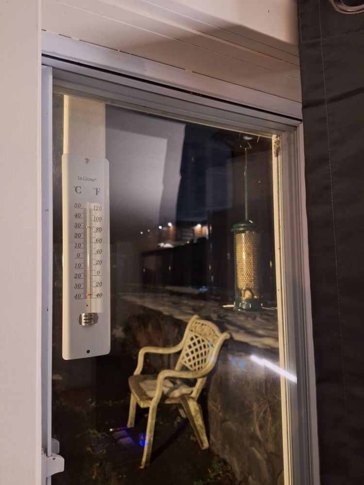 Same thermometer now hanging from the piece of wood on a tight screw, outside my living room window. A bird feeder is also in the same window beside the thermometer.