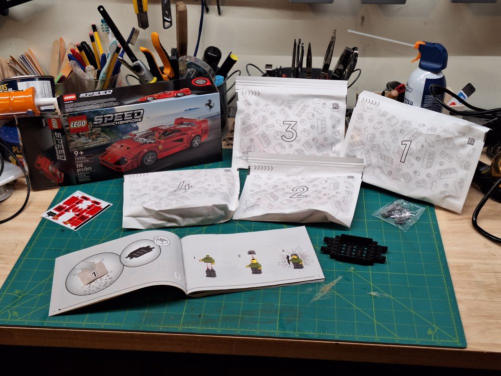 A Lego kit with its 4 bags laid out on a workbench. The booklet is open on page 1. The final piece will be a red Ferrari supercar.