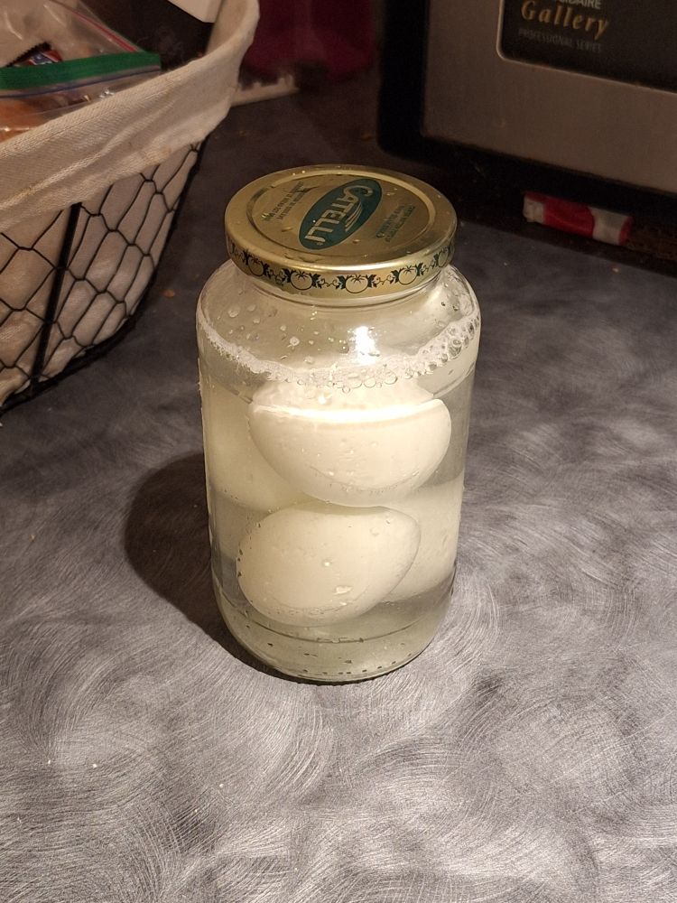 A large glass jar containing 6 eggs soaking in a mix of mostly water with some vinegar and salt (i have no idea wth i'm doing)