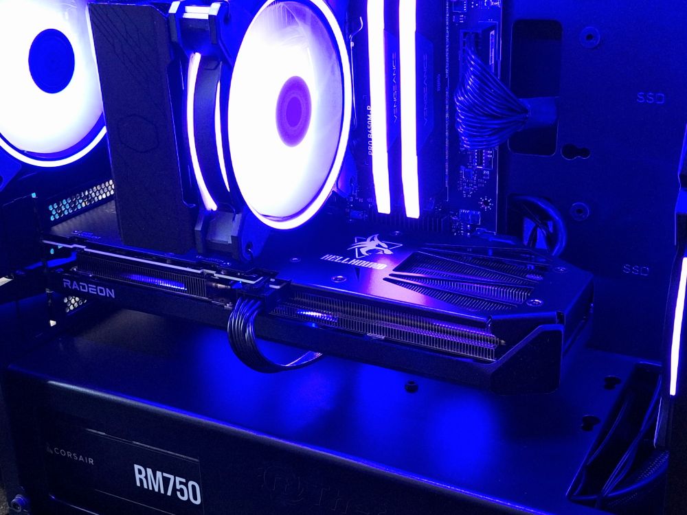the inside of a gaming pc tower, all black with purple rgb lighting. a brand new triple fan gpu is in the middle with a lit-up air cooler and ram above it.