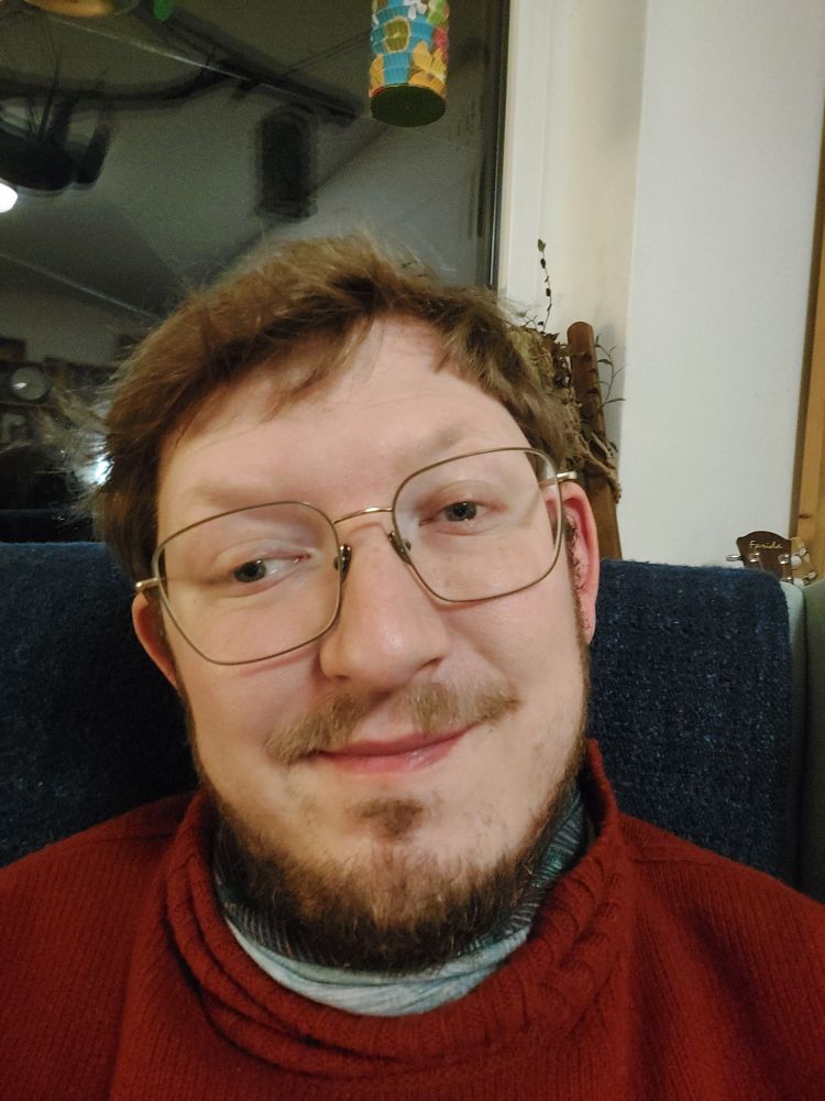 a selfie of me, a mid thirty white man with glasses and a beard. I am wearing a red sweater. I am in my living room