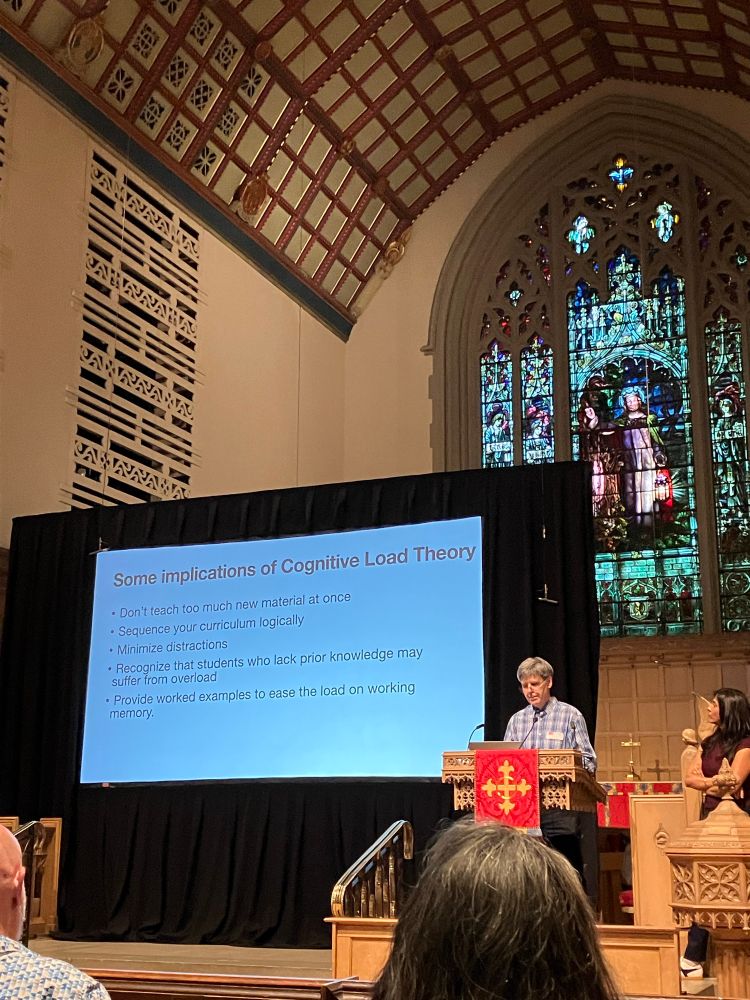Drs. Sachdeva and Hewitt in front of a slide about implications of cognitive load theory. 