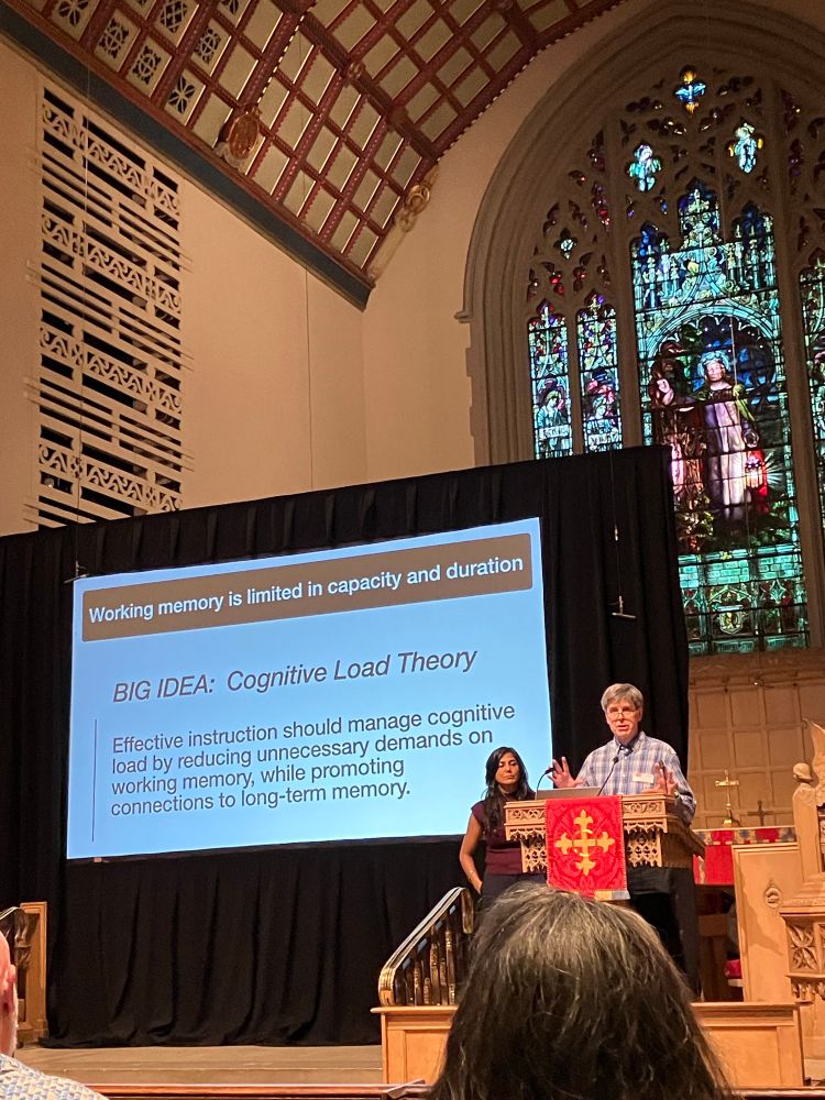Drs. Sachdeva and Hewitt in front of a slide about cognitive load theory. 