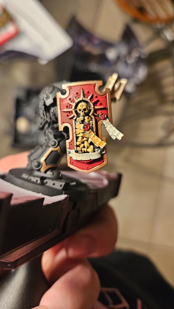 Blood Angel Space Marine Chaplain in Terminator Armor with a relic shield painted red and gold. With the bones of a fallen comrade being brought to bear so that he sees battle once more.