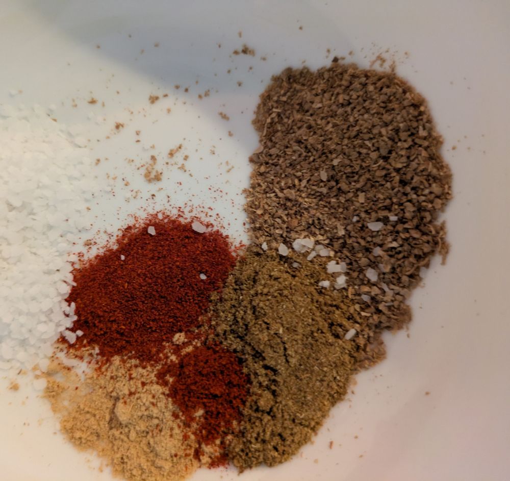 A photo of a bunch of ground up spices and part of a small pile of salt in the bottom of a white bowl. From the top right going clockwise is roasted, ground coriander, then toasted, ground cumin. Pile of yellowish dried ginger with some ground paprika and a smaller pile of Cayenne pepper. There's salt budding right up against those colors, but most of it is cut off in this shot. The browns and reds and yellow are very satisfying and autumnal.