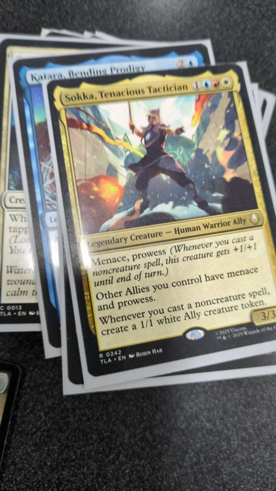 A stack of magic the gathering cards with a card on top that is a 3/3 blue, red, and white legendary creature called Sokka, Tenacious Tactician. He does cool stuff to allies.