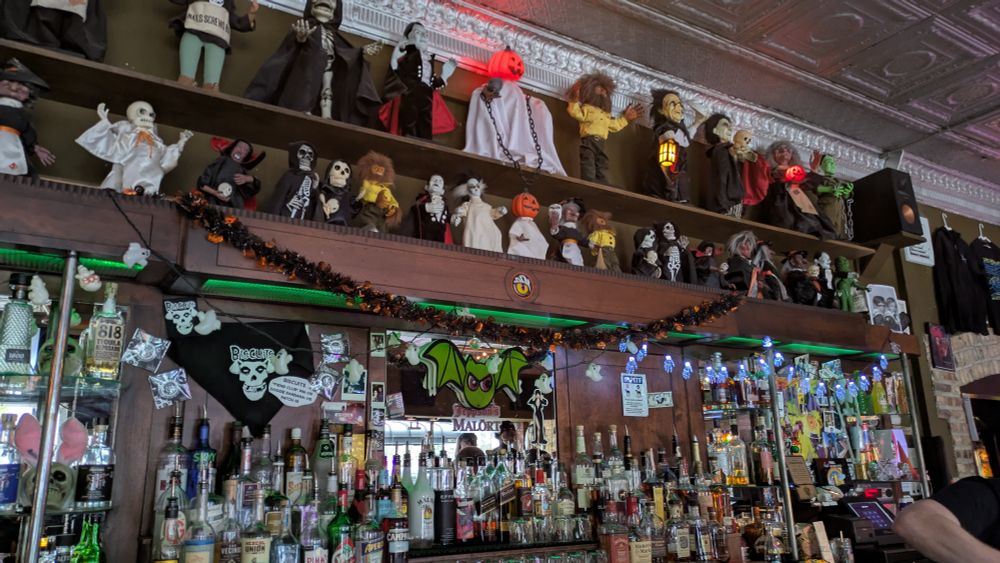 A photo of a display of items behind a bar, including liquors and Halloween decorations and a collection of spooky dolls