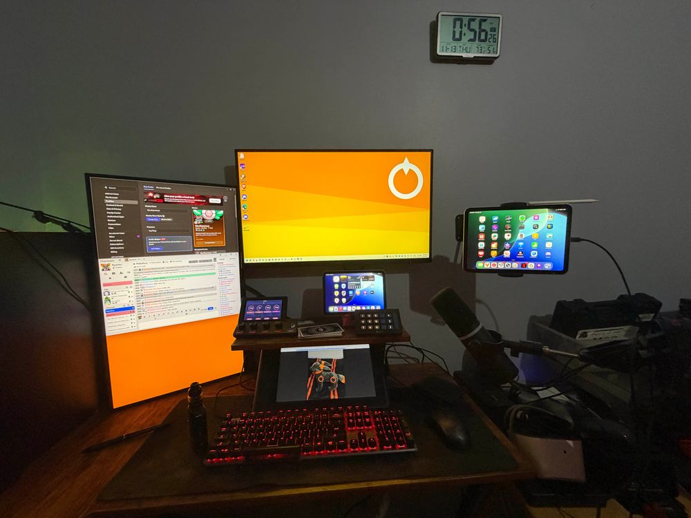 The bweh setup! There is a monitor affixed to the wall, another monitor in vertical position to its left, a graphics monitor below a hutch, a mini iPad, audio controller and stream deck above the hutch with tarot cards, and a mounted iPad to the right of the main monitor.