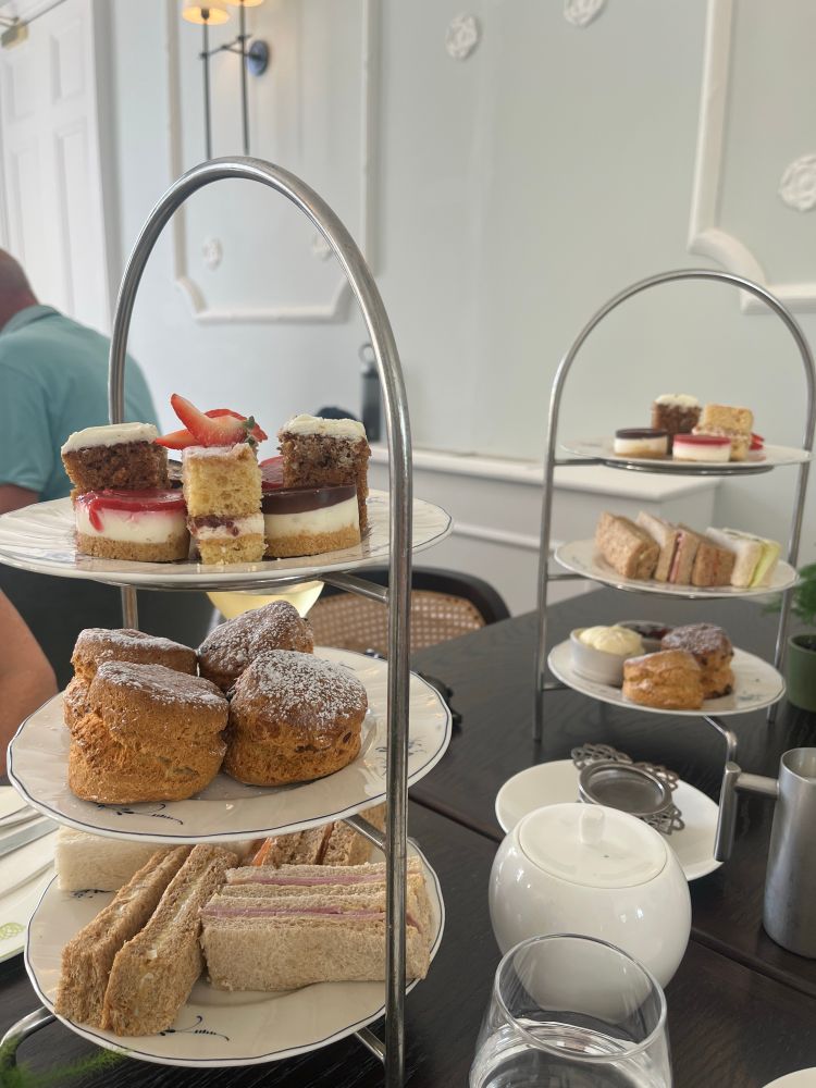 Three tier afternoon tea - sandwiches on bottom, fruit and plain scone on second layer and a selection of small cakes on the top. 