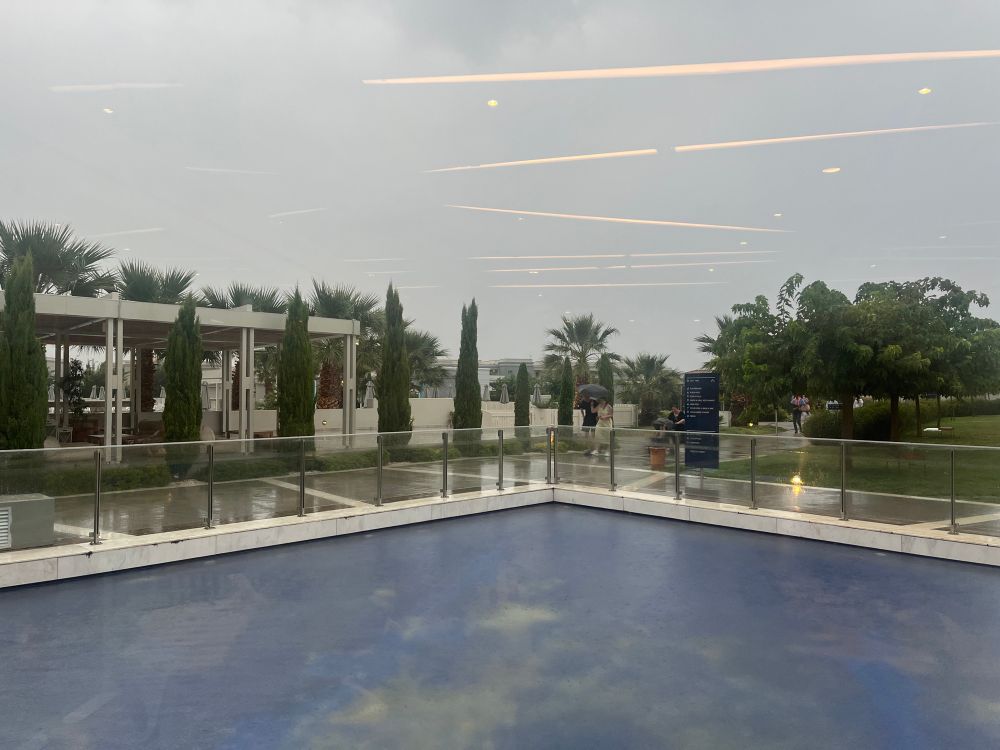 A very grey sky, rain pouring, wet paths and people holding umbrellas. 