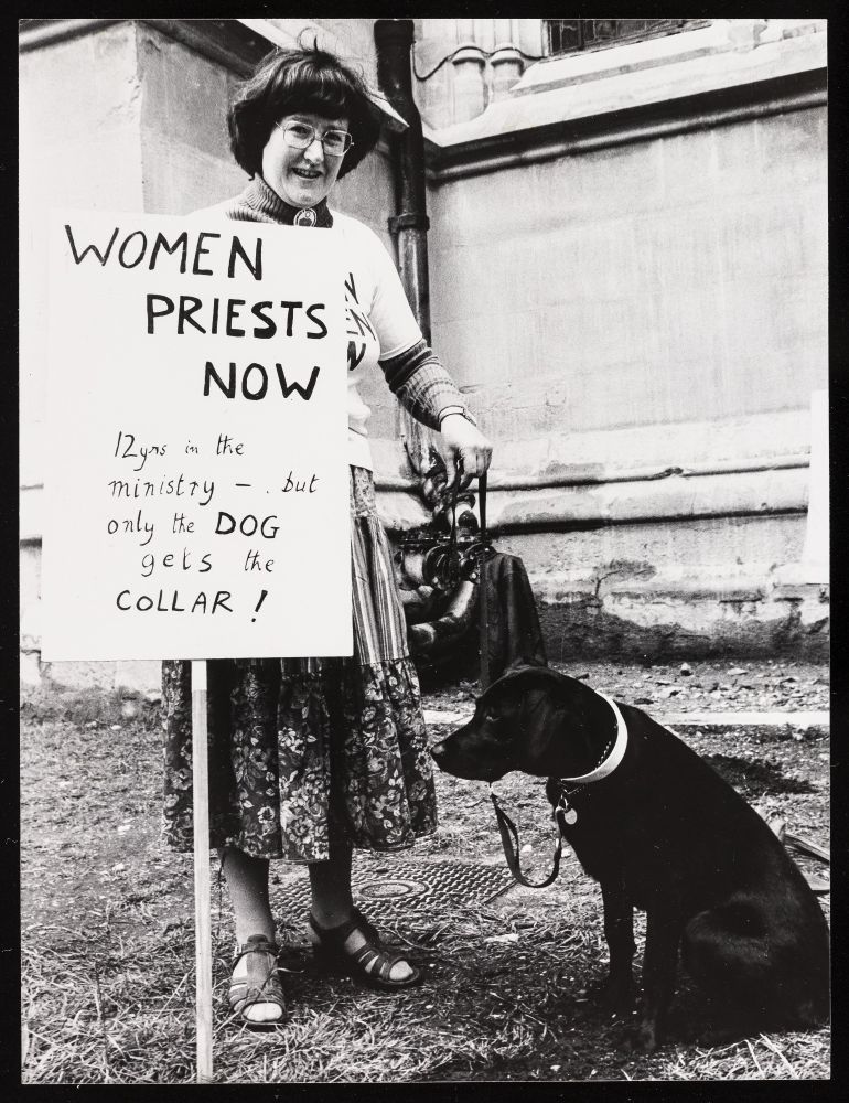 woman holding placard next to dog . placard reads 12 years in the ministry but only the dog get the collar.
