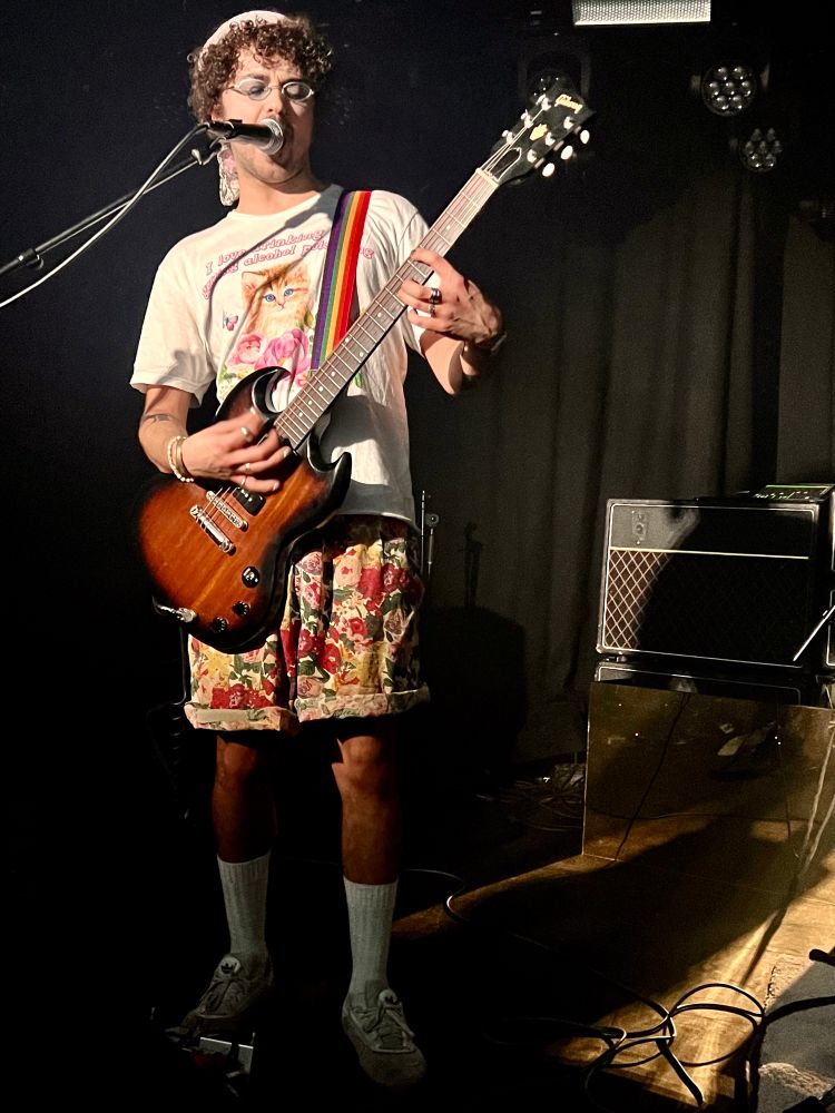Een gitarist in fleurig shirt met wild bedrukte korte broek 