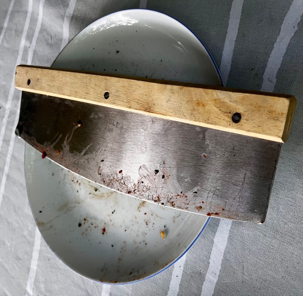 Een groot pizza mes met houten handvat ligt op een wit bord. Het mes is gebruikt 