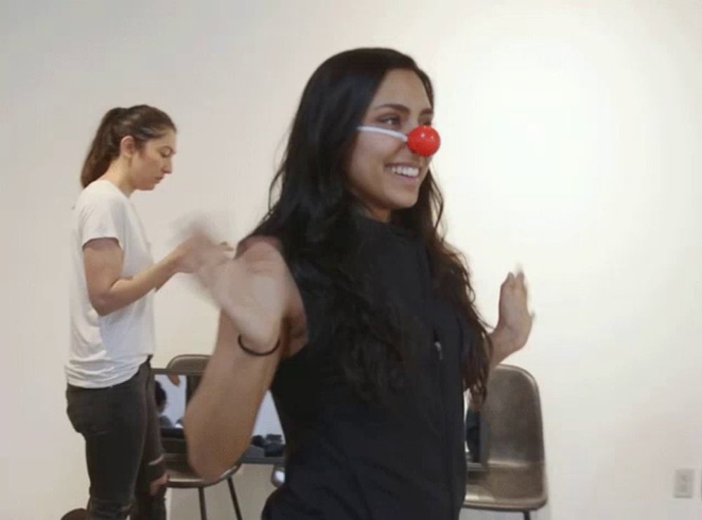 a woman wearing a red clown nose smiles while another woman watches