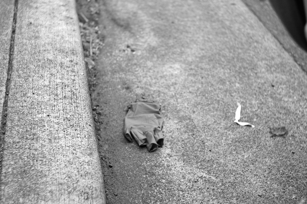 A black and white photo of a rubber glove on the pavement next to a curb.