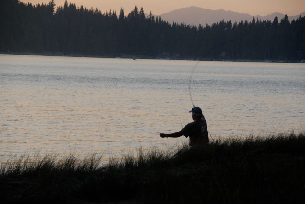 Silhouette of a fisherman casting as dusk deepens
