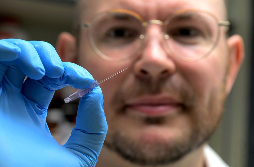 Shown is Dr. Baylink holding a tiny glass needle known as a microcapillary. This was used to study chemotaxis by injecting chemical effectors into a pond of motile bacteria and monitoring their responses through microscopy.