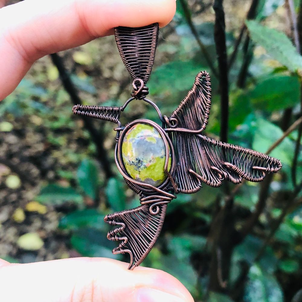 Copper wirewrapped pendant in the shape of a hummingbird with a green stone body & weaved head, wings, beak, and tail. 