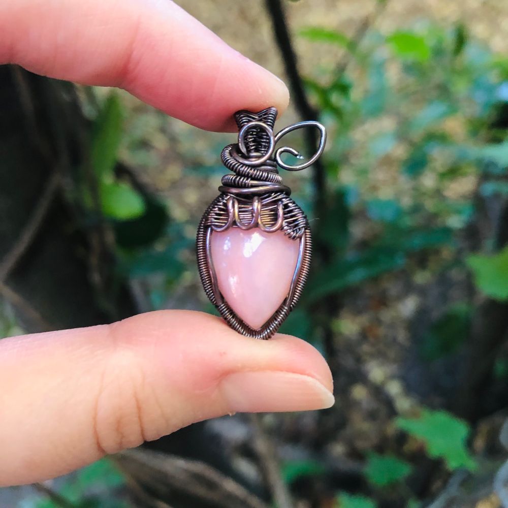 Copper wirewrapped pendant in the shape of a strawberry with a light pink stone and little wire leaves 