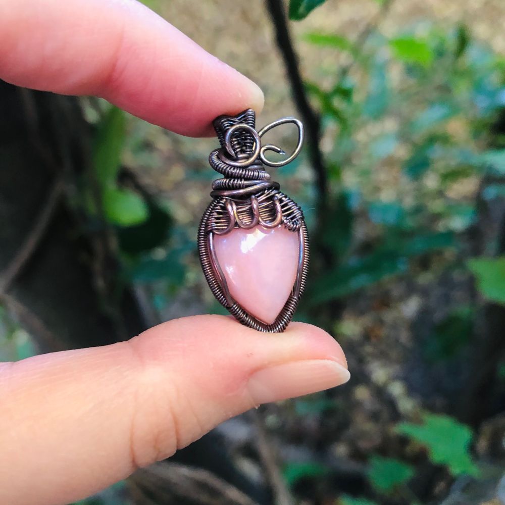 Copper wirewrapped pendant in the shape of a strawberry with a light pink stone and little wire leaves 