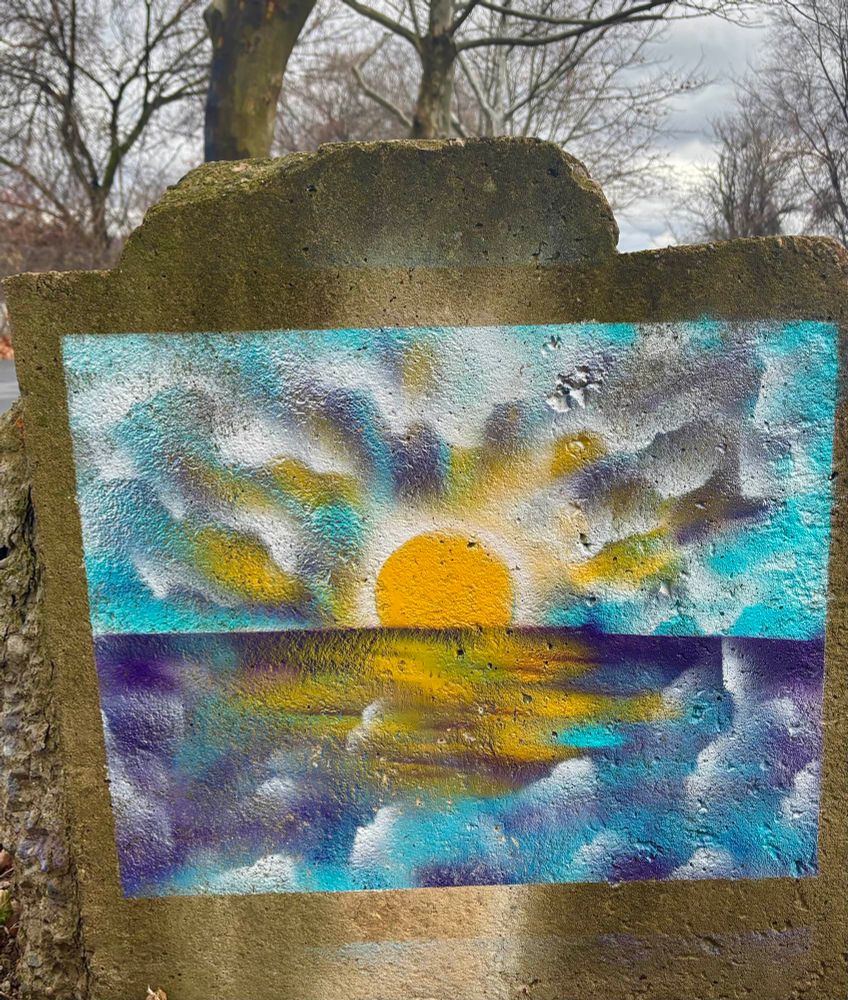Pastel somewhat surrealist c
painting of a sunset (or sunrise?) over the ocean located on a stone concrete barrier sitting in front of a couple bare trees 