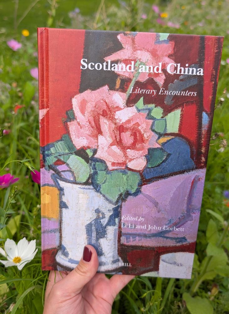 Holding the book "Scotland and China" amidst a meadow in bloom