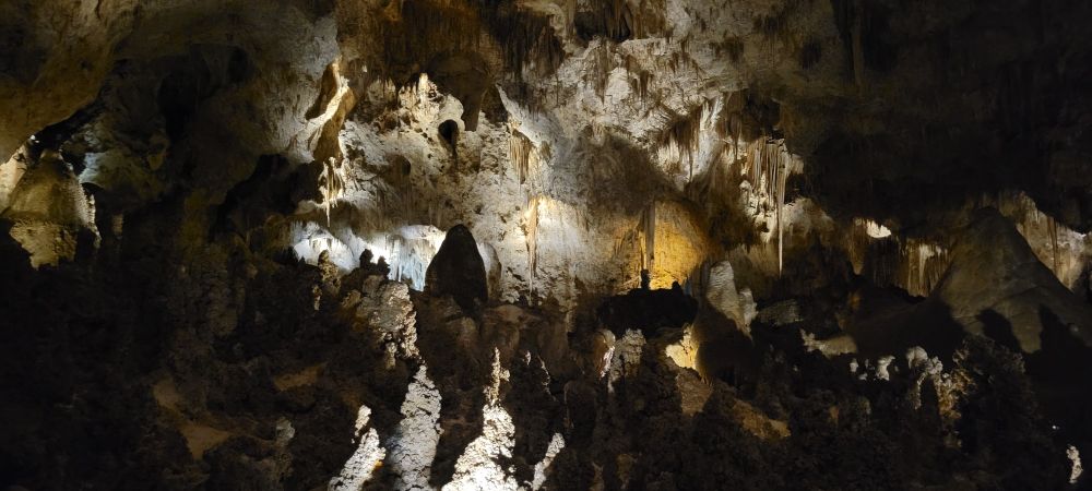 A massive cavern filled with a variety of stalactites and stalagmites, most of which are far larger than a person.  Some are illuminated while others are silhouetted.