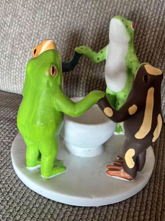A candleholder depicting four frogs of different species holding hands in a circle looking up the candle.